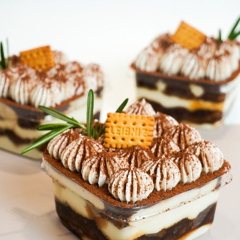 Tiramisu cups garnished with cream swirls, cocoa powder, biscuits and rosemary sprig