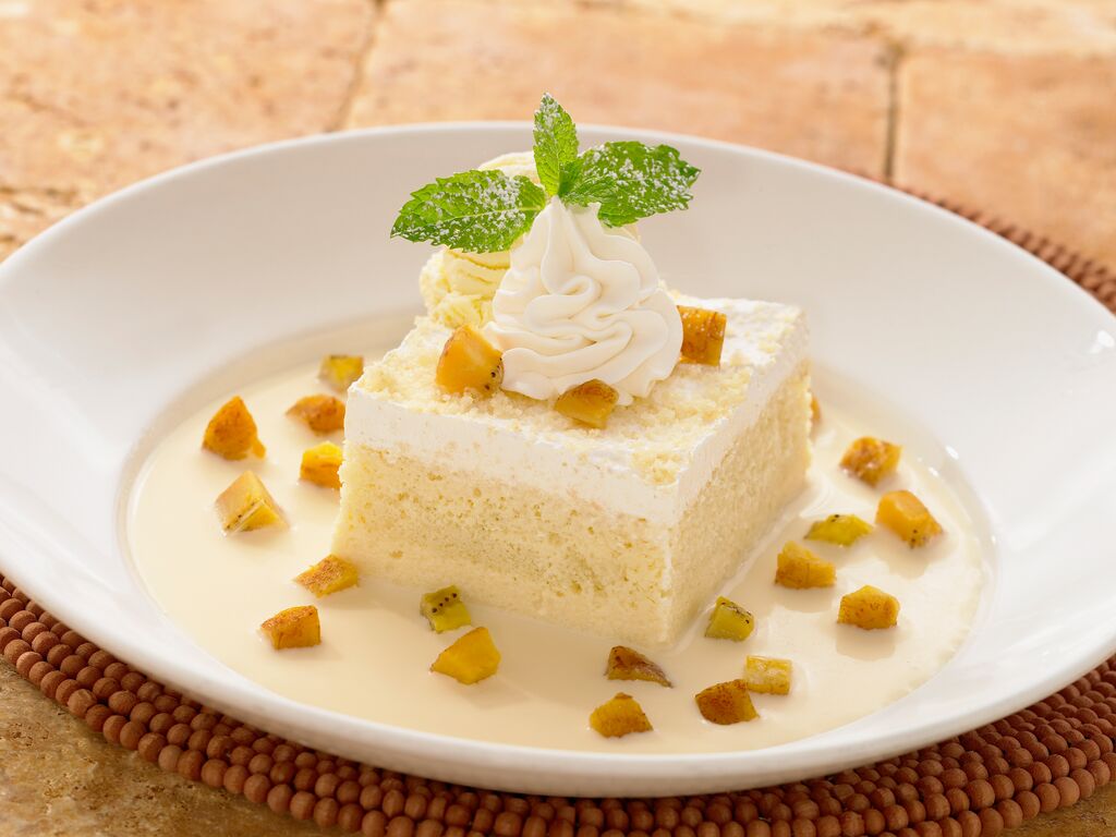 Vanilla sponge cake topped with whipped cream, mint leaves, and diced mango pieces on a white plate
