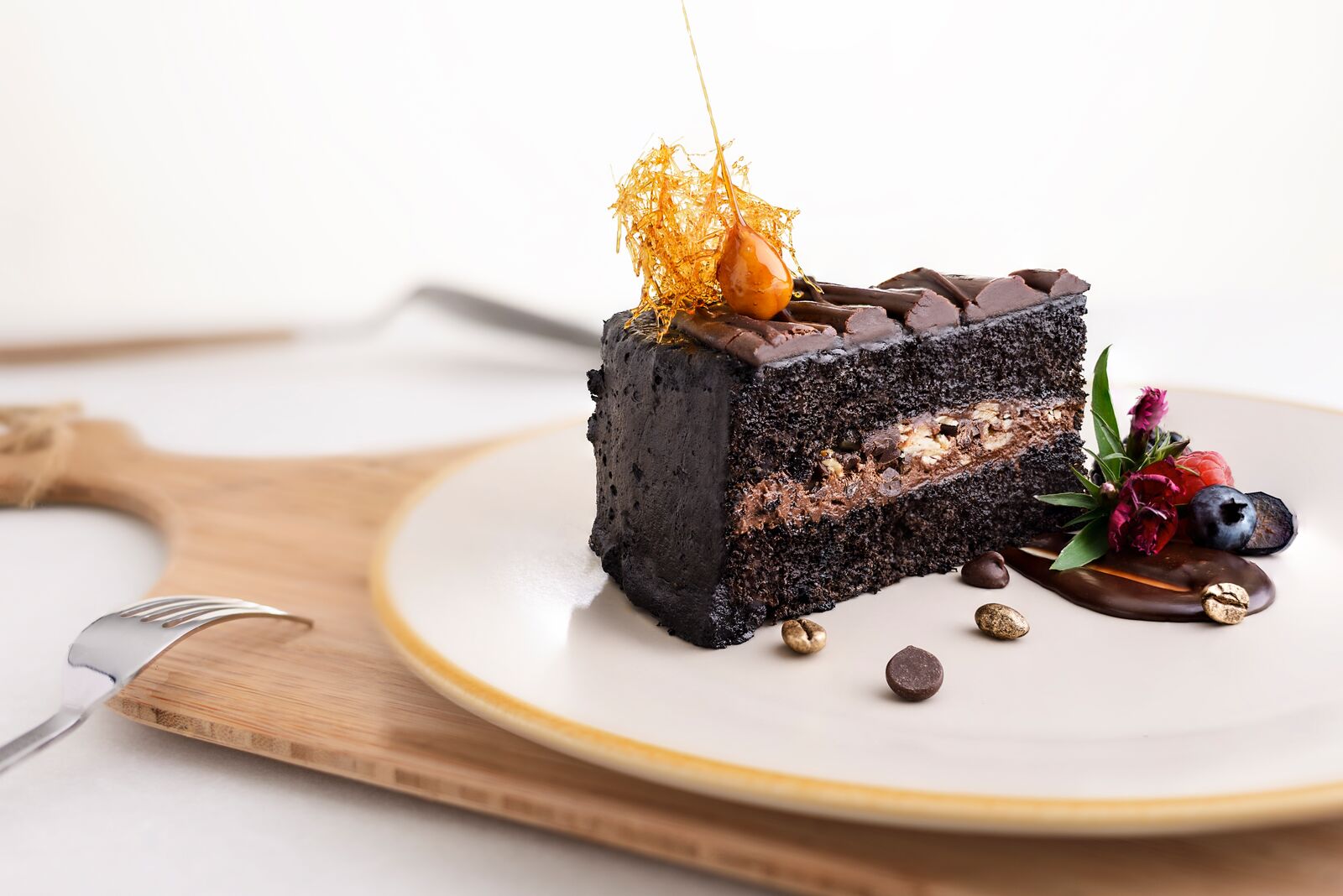Chocolate cake slice with cream filling, chocolate glaze and fruit garnish.