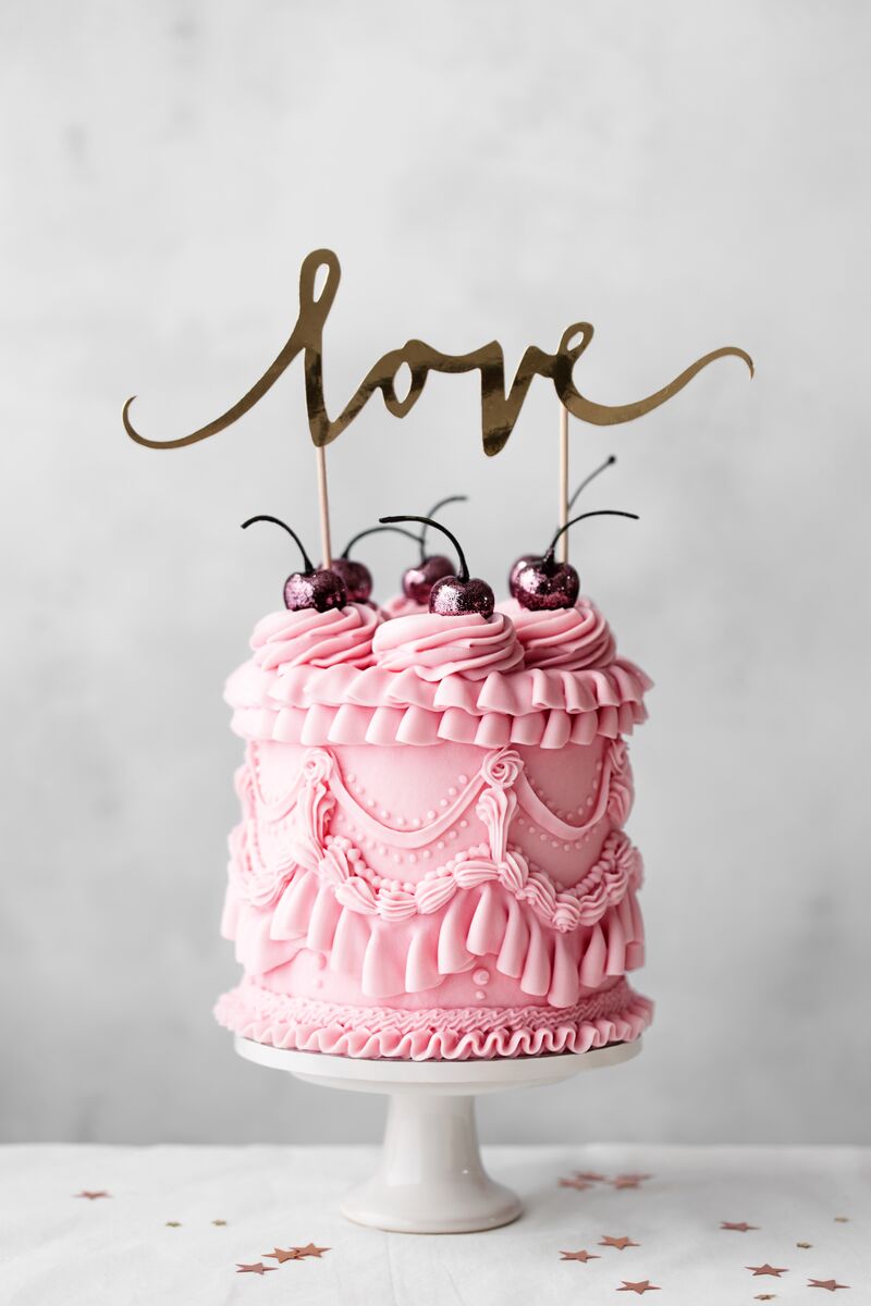 Pink vintage-style cake with cherries and ornate cream decoration.