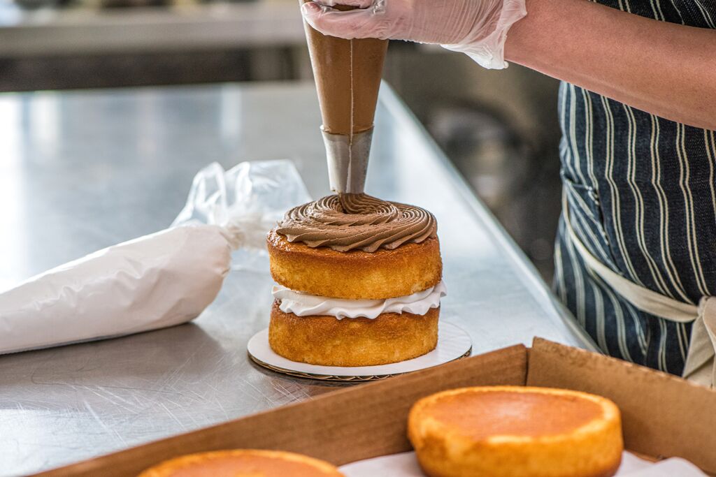 Baker piping ganache onto stacked sponge layers while preparing a celebration cake