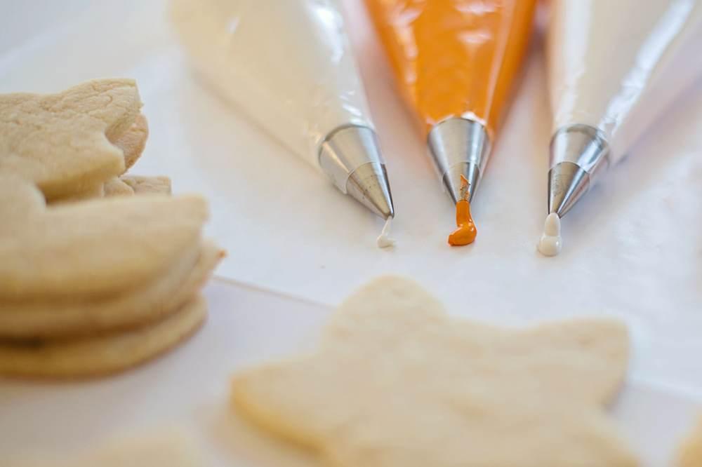 Three piping bags fitted with metal piping nozzles beside cookies