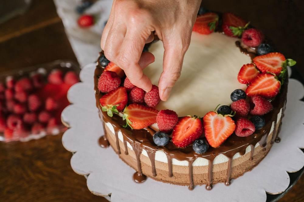 Baker decorating a celebration cake with fresh berries and a chocolate drip