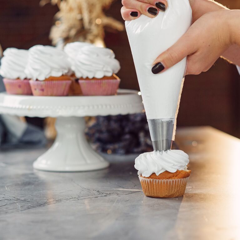 Homebaker piping a buttercream swirl onto a cupcake using a piping bag and star nozzle