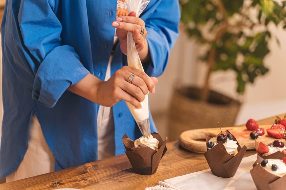 Person piping cream onto a chocolate cupcake.