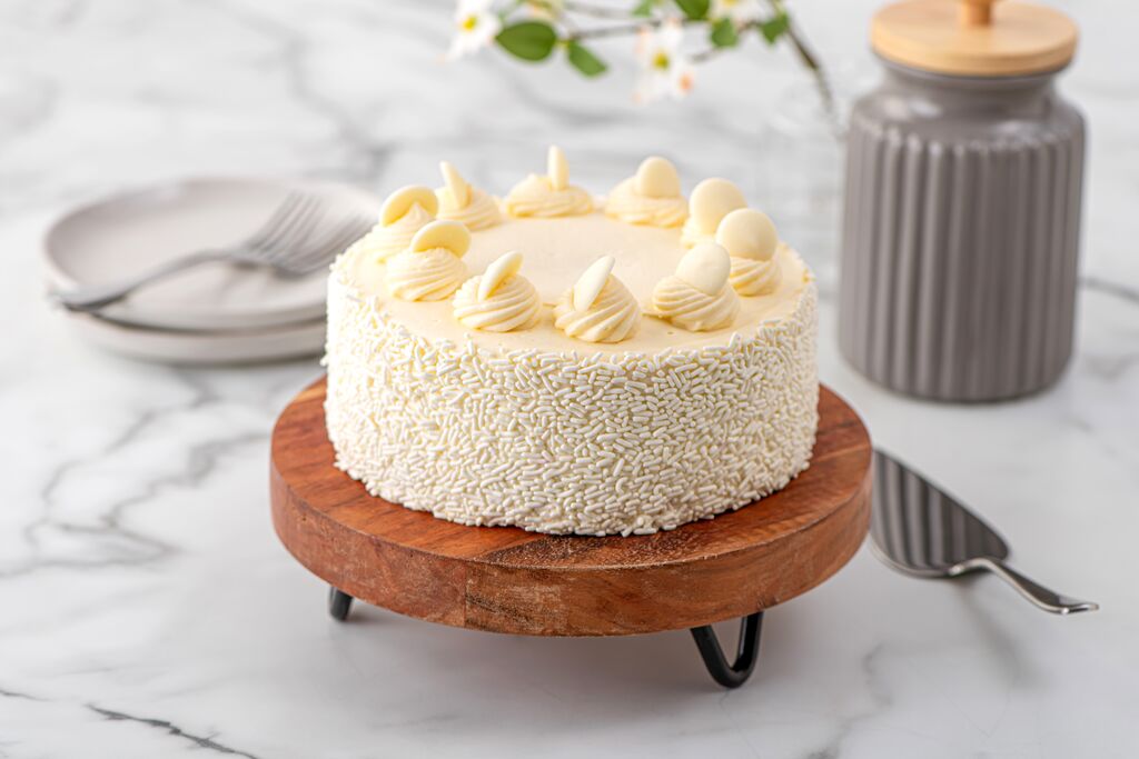 White frosted cake with sprinkle-covered sides and piped rosettes