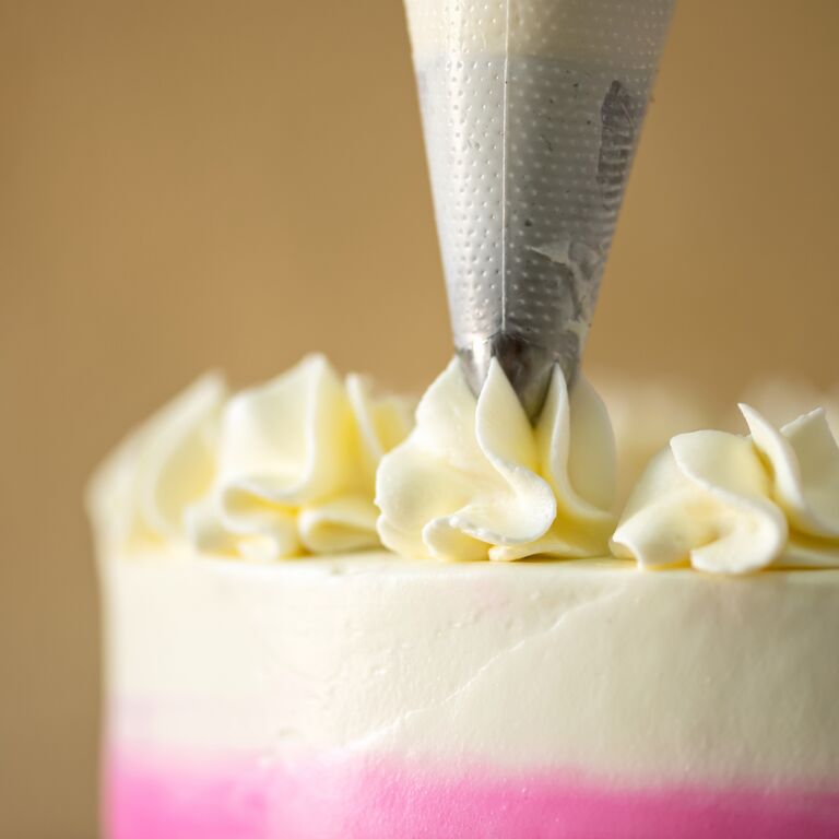Piping bag with star nozzle making frosting rosettes on a cake