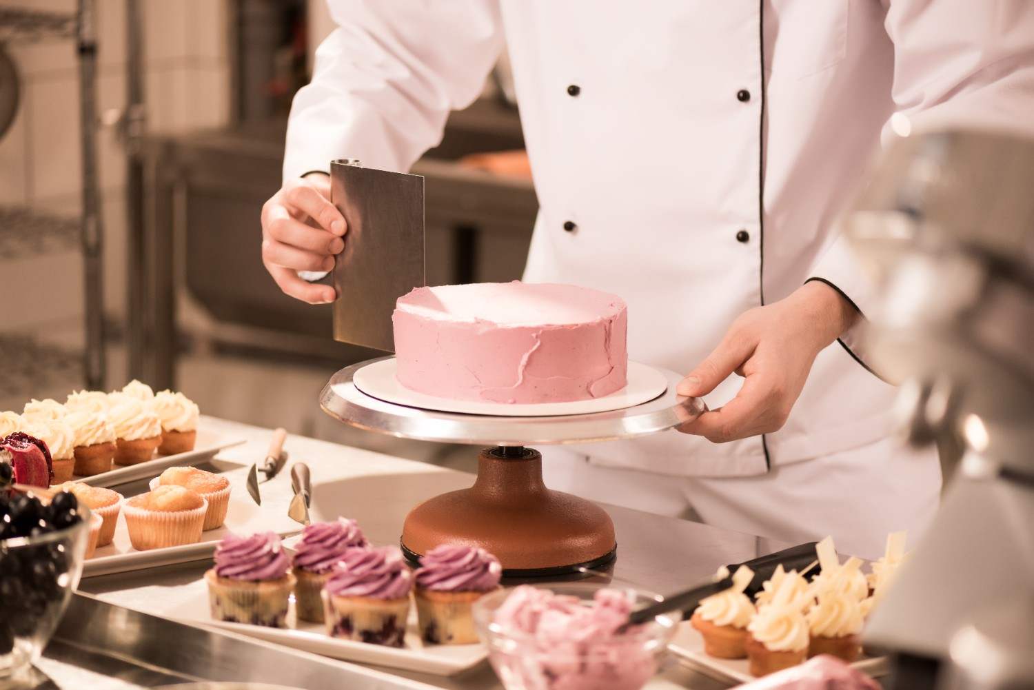 Chef smoothing pink frosting on a cake with a bench scraper and turntable